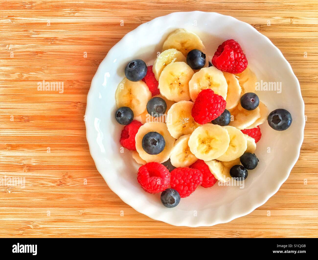 Bowl of yogurt topped with fresh banana, blueberries and raspberries on a bamboo board with copy space - Smartphone Captured Stock Image