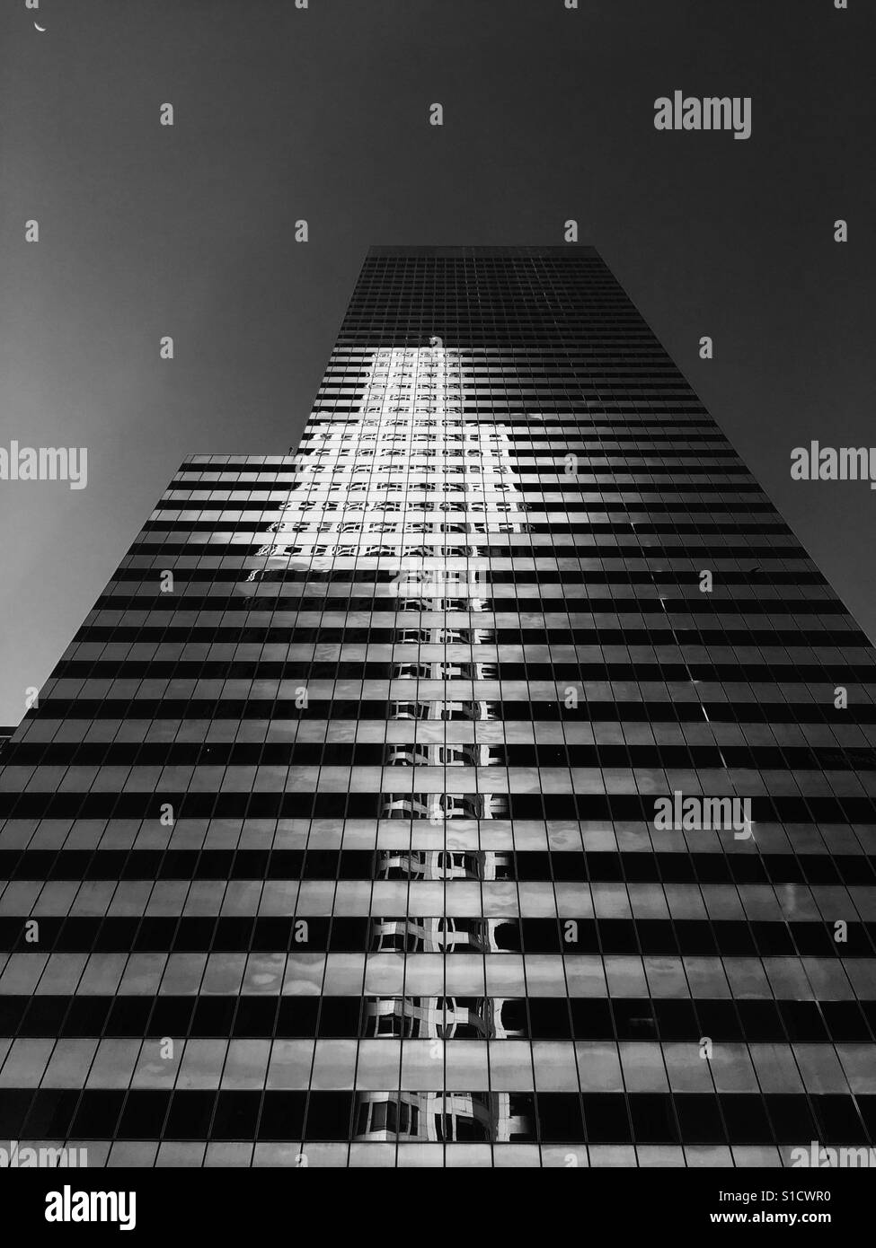 Abstract architecture of a tall skyscraper with light reflected on surface and moon in corner Stock Photo