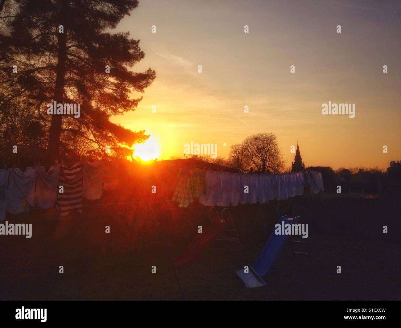 The sun starts to drop in the sky at early sunset, hiding behind a washing line full of hanging clothes. - Smartphone Captured Stock Image