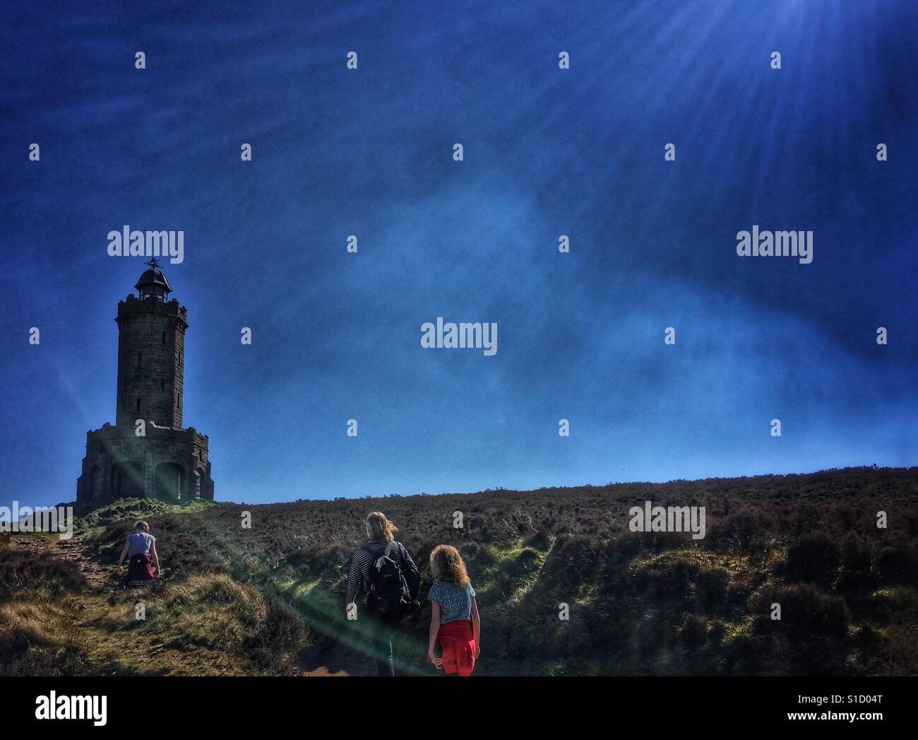Family walking towards Darwen Jubilee Tower on Darwen Moor backlit by the sun Stock Photo