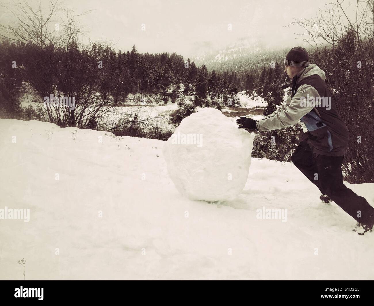 Young man pushing a large snowball up a hill. Faded edit. - Smartphone Captured Stock Image