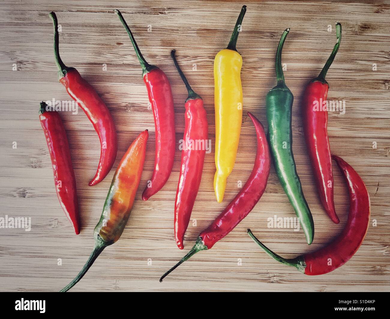 Green, yellow, orange, red hot chilli peppers on a bamboo chopping board - Smartphone Captured Stock Image