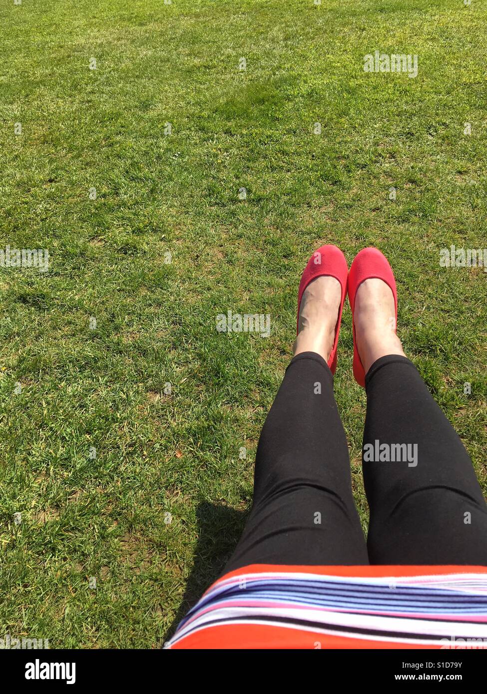 Woman's legs stretched out over green  grass lawn on a warm and sunny spring day. Stock Photo