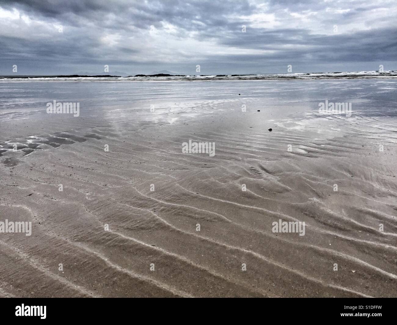 Ridges in sand and glow of light in the shallows of the sea in Cymyran beach, Rhosneigr, Anglesey, North Wales, - Smartphone Captured Stock Image