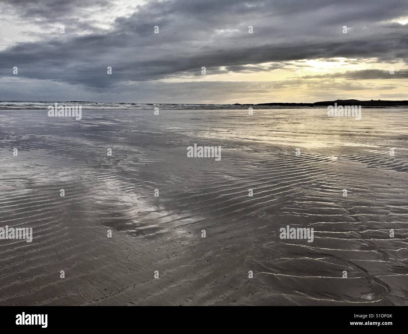 Dusk on Cymyran beach with glow of light over the west coast of Anglesey, North Wales - Smartphone Captured Stock Image