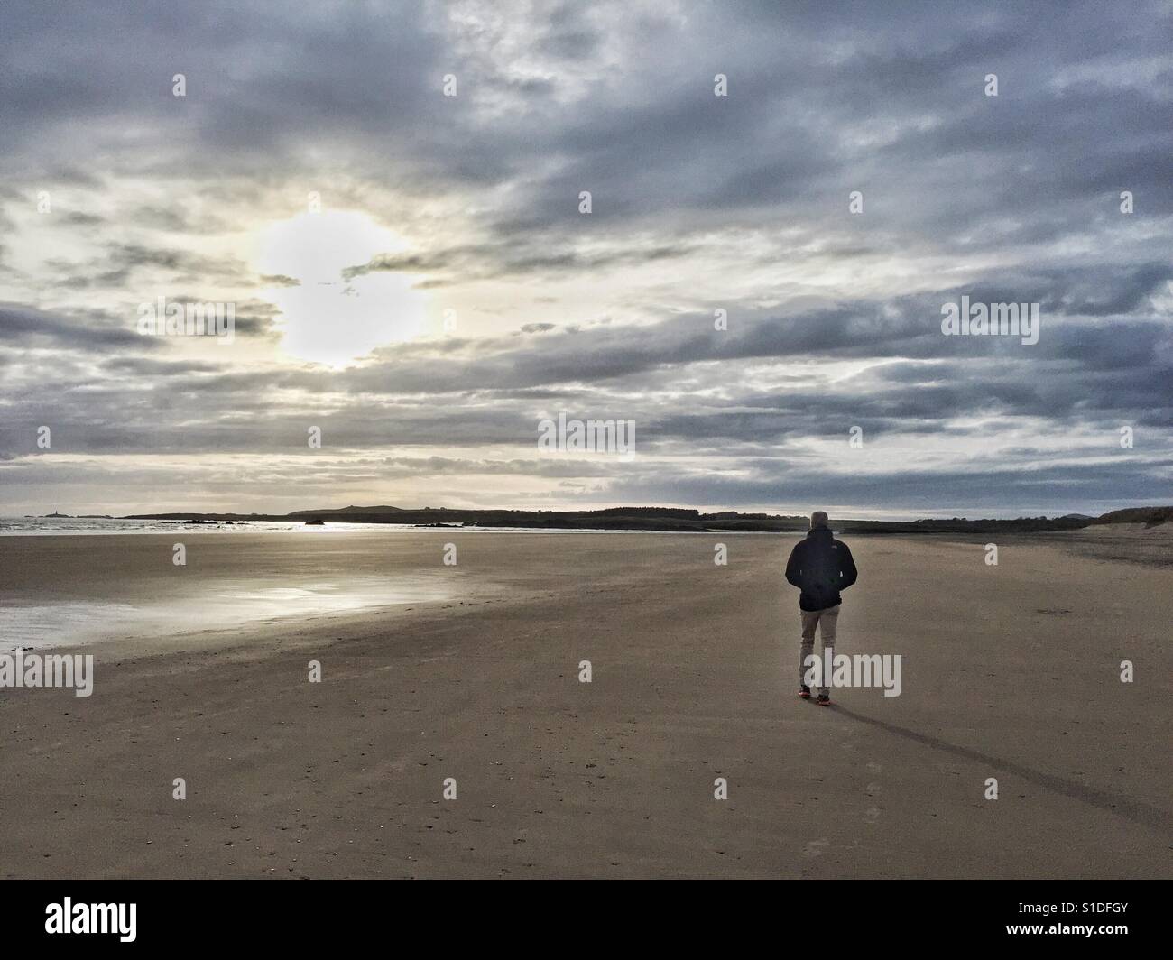 Man walking along an otherwise empty Cymyran beach as the sun sets, Anglesey, North Wales - Smartphone Captured Stock Image