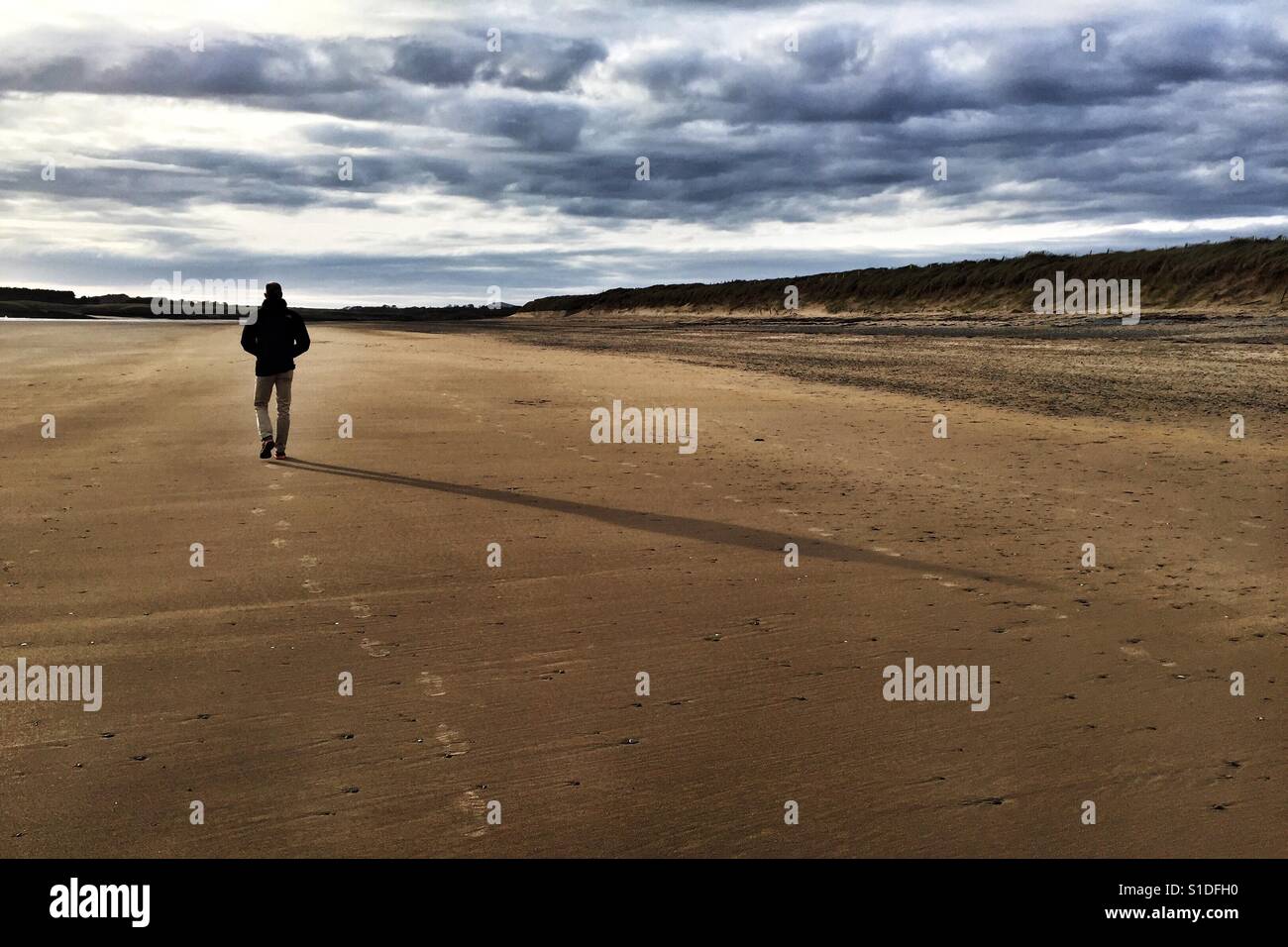 Man walking alone on Cymyran beach, Anglesey, North Wales - Smartphone Captured Stock Image