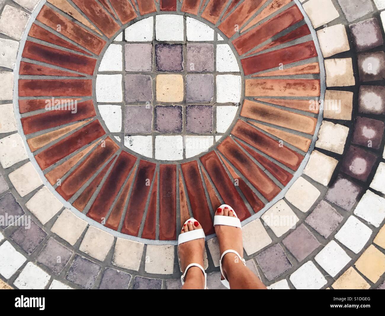 View of feet on a circle floor mosaic - Smartphone Captured Stock Image