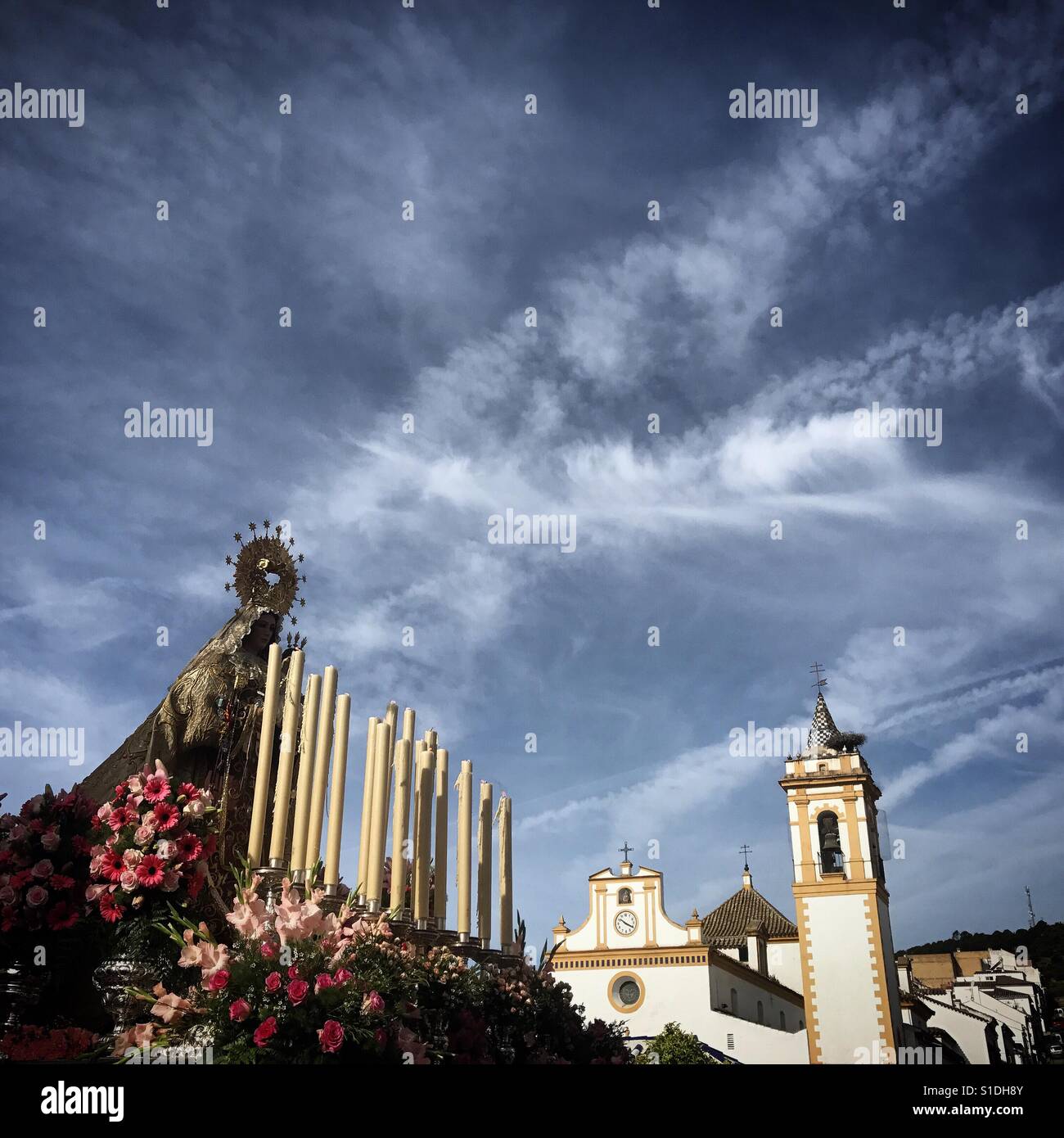 An image of the Virgin of Carmel is displayed during Easter Week under a sky covered by plane trails ( known as chemtrails) in Prado del Rey, Sierra de Cadiz, Andalusia, Spain - Smartphone Captured Stock Image
