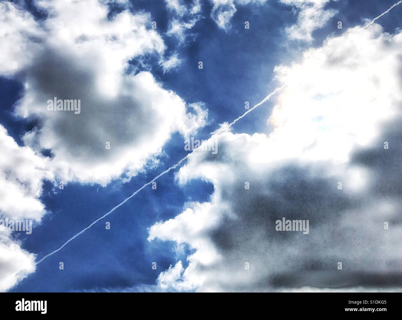 Jet Stream , the trail of a jet aircraft diagonally crossing a cloudy sky with patches of blue Stock Photo
