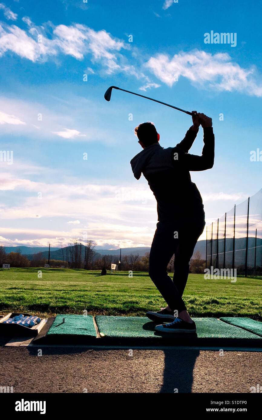 Young man wearing Street clothes practicing his golf swing at a driving range. Stock Photo