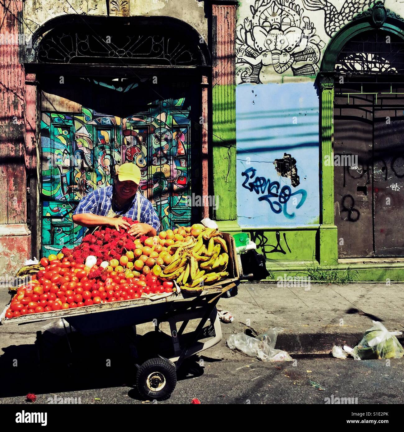 A Salvadoran man sells fruits in front of a ruined house with Spanish colonial architecture elements, painted over by a local artist, in the center of San Salvador, El Salvador, 12 November 2016. Stock Photo