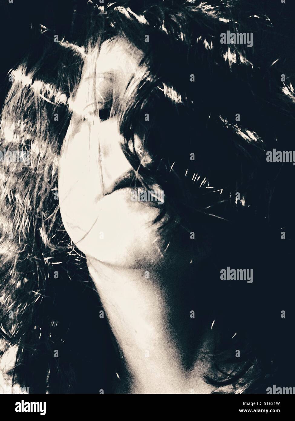 Black and white woman's head portrait with her hair covering her face and shining light beams Stock Photo