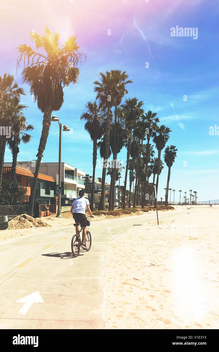 Sunny Southern California March weather on the beach as a teenage boy is riding a bike on the Strand Bicycle Beach Path. March 2017. Stock Photo