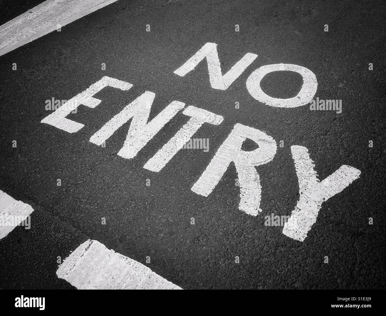NO ENTRY. White stencilled letters on a tarmac (asphalt) road instructing travellers that they are not permitted to proceed past this point. A conceptual image. Photo Credit © COLIN HOSKINS. - Smartphone Captured Stock Image