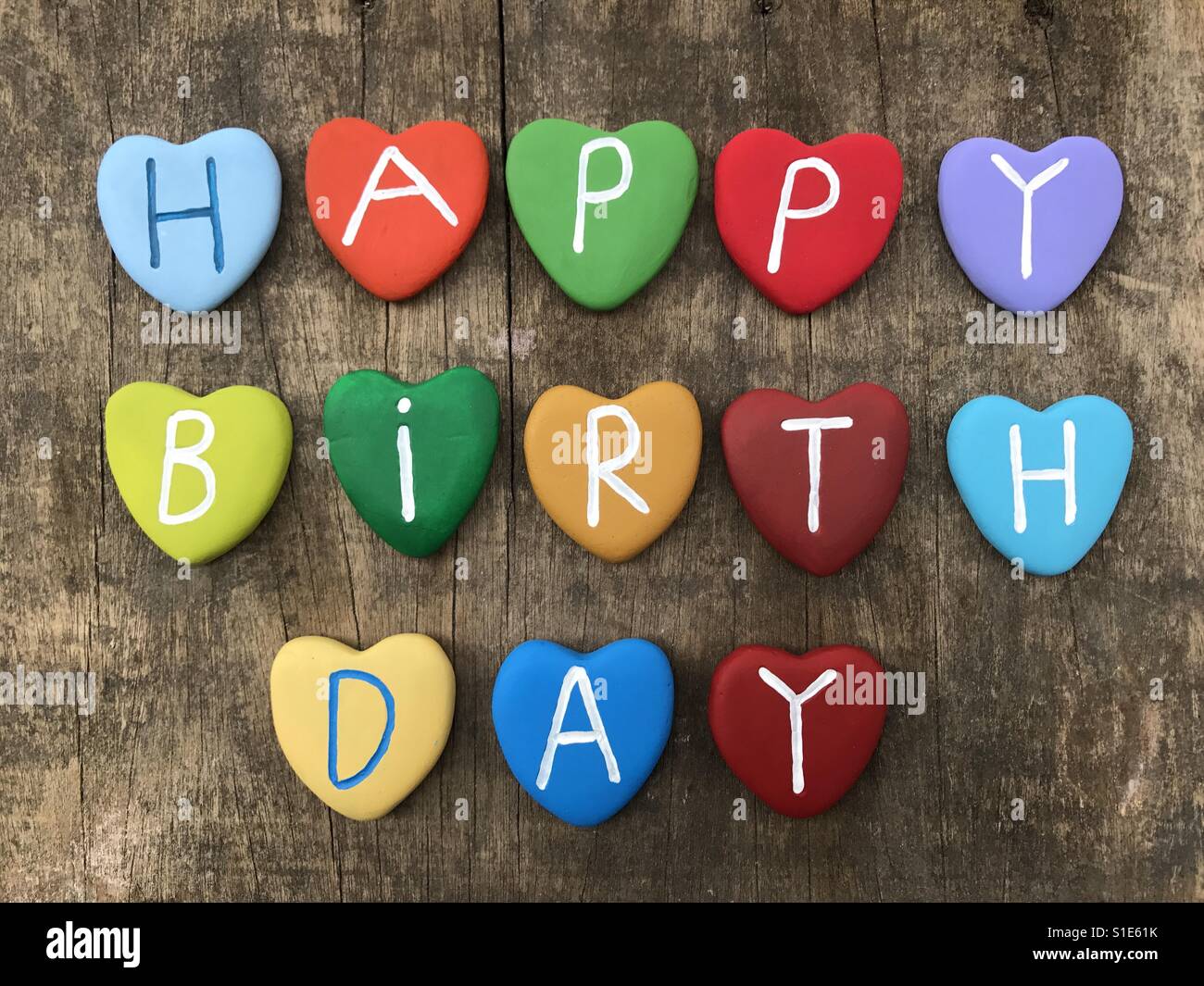 Happy Birthday with multicolored heart stones over  wooden raw board Stock Photo