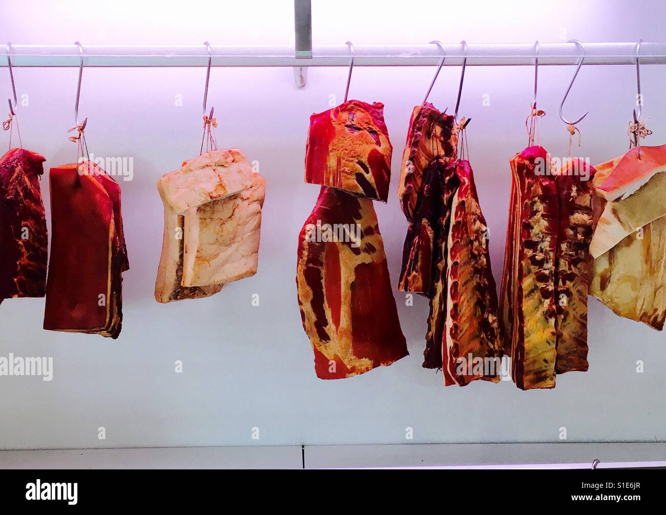 Dry aged meat hanging from hooks at a butcher Stock Photo