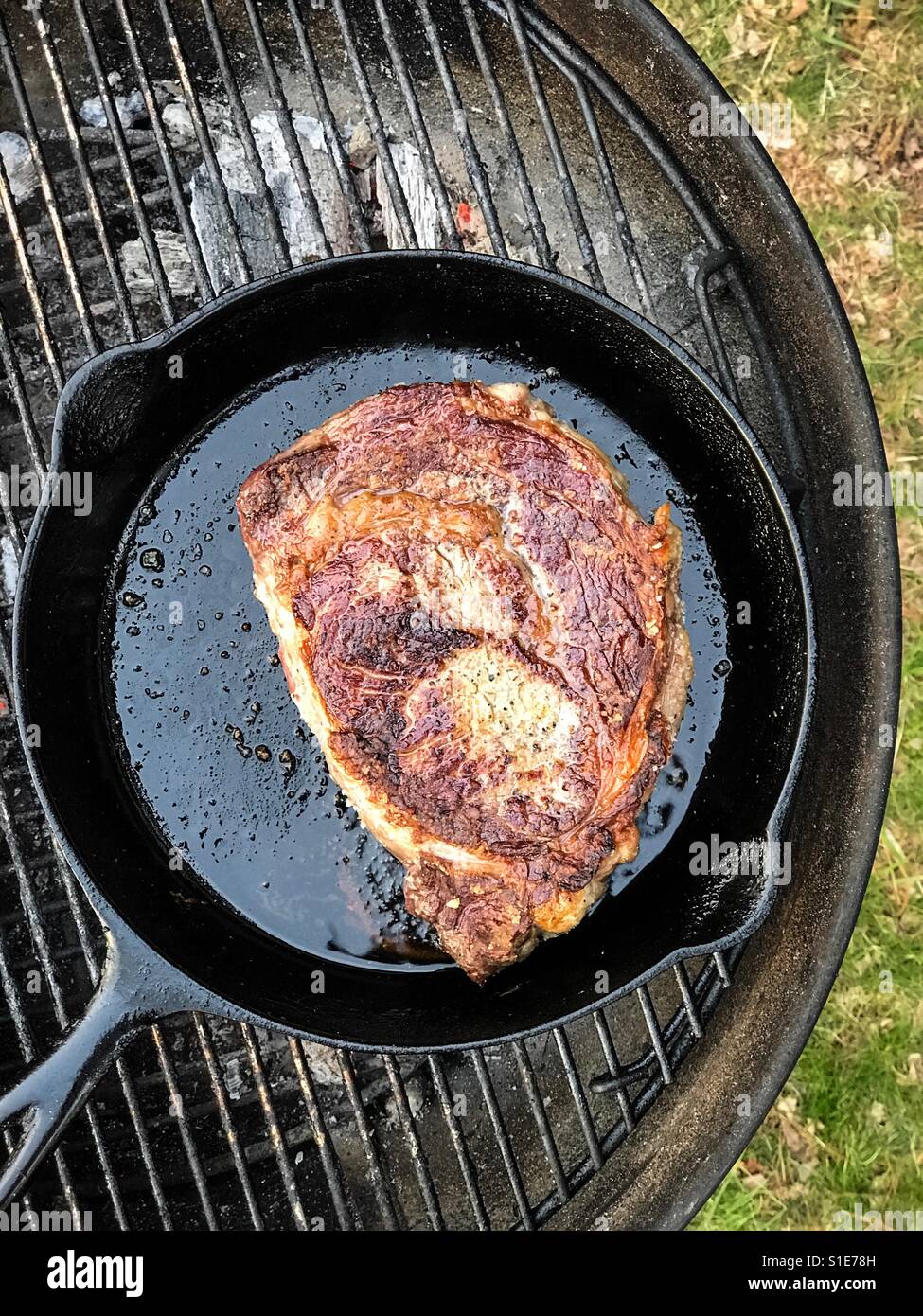 Cooking steak in a skillet on a charcoal grill. New Jersey, USA Stock