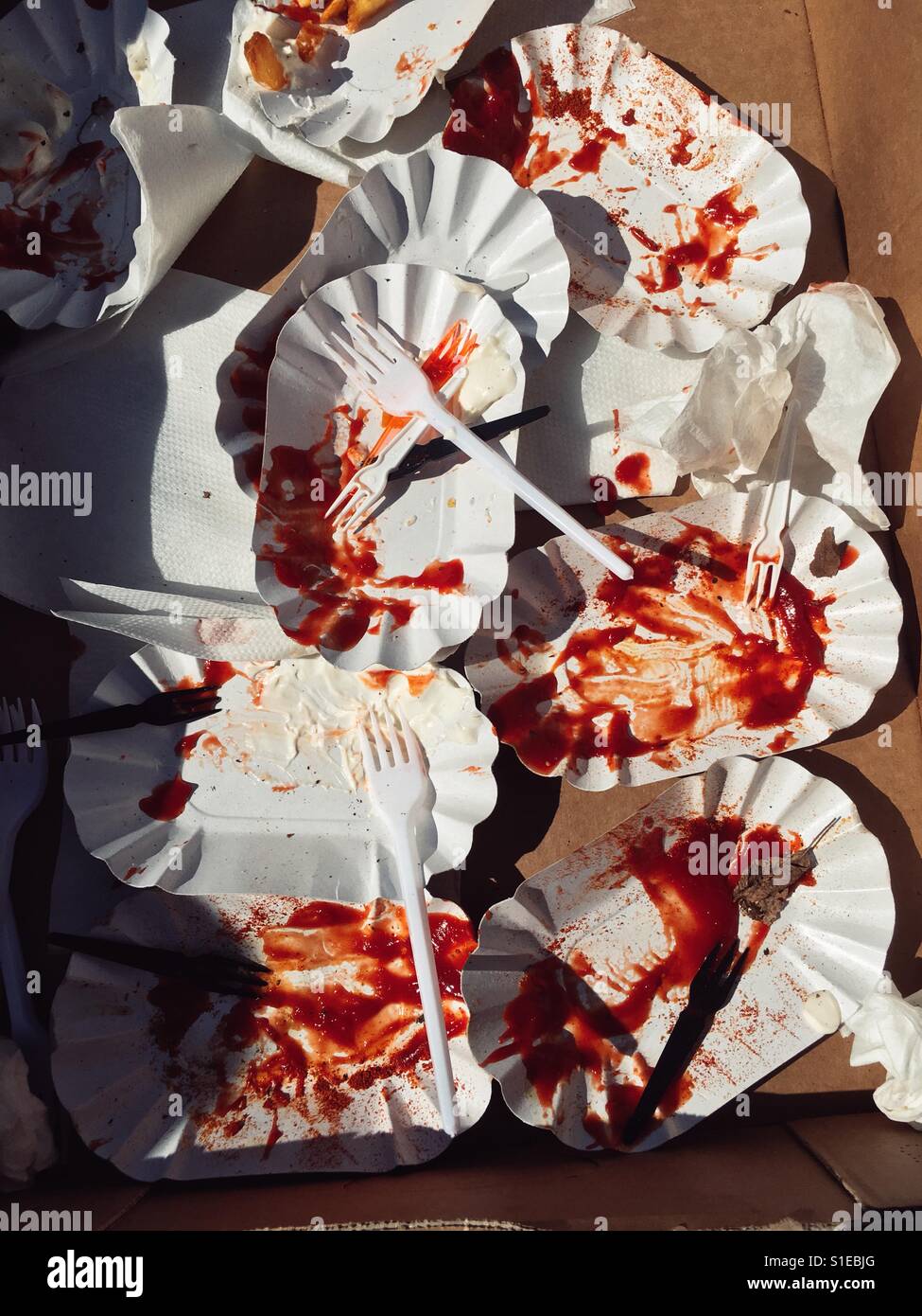 Leftovers of a meal of fries with ketchup and Mayonnaise and curry sausage on paper plates with plastic forks Stock Photo