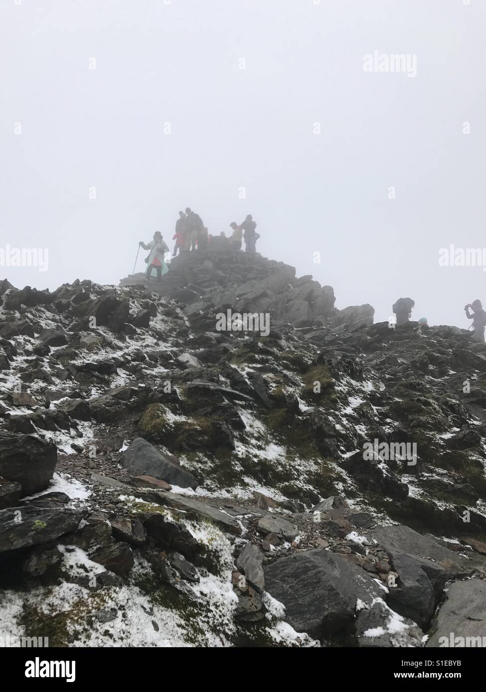 People on the peak of Mount Snowdon in the cloud with snow on the ground Stock Photo