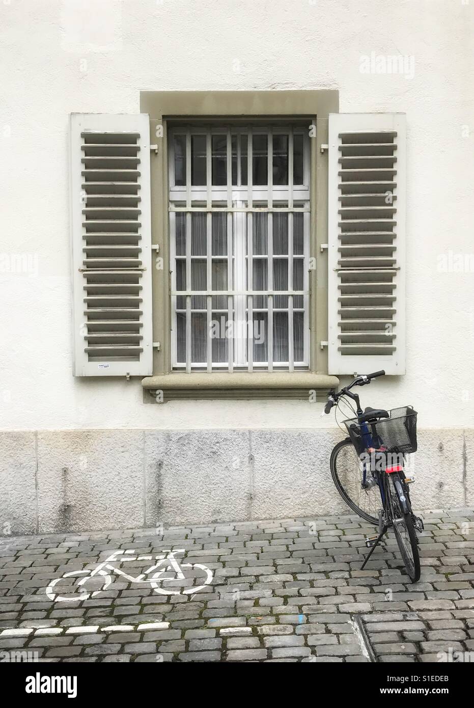 Bicycle parked on cobblestone pavement under window with security bars and shutters in Berne, Switzerland Stock Photo