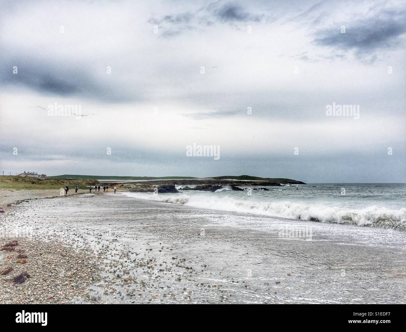 Big sea with breakers and people walking along the beach on coastline of Anglesey, near Rhosneigr, Llanfaelog, Maelog, North Wales, UK - Smartphone Captured Stock Image