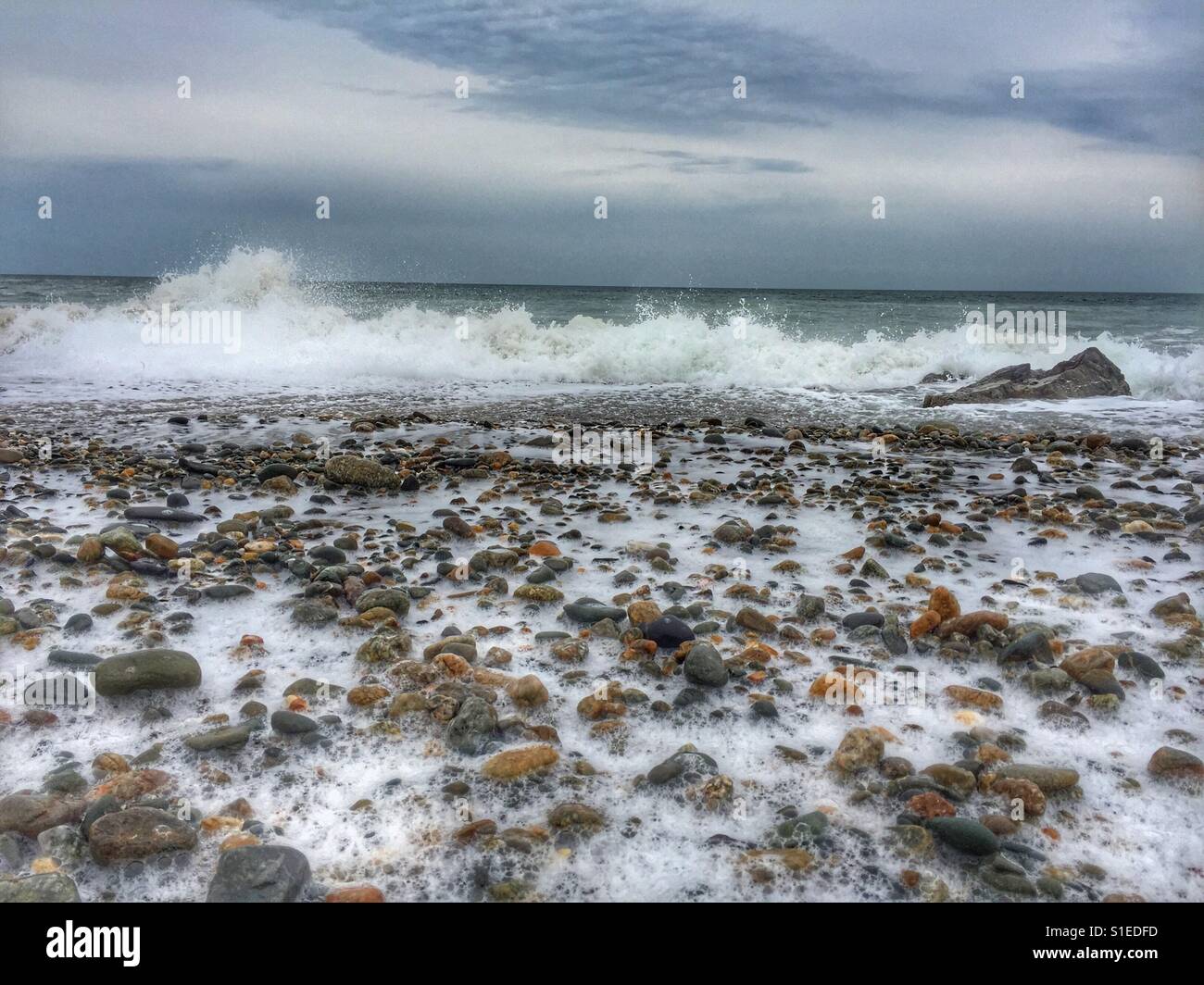 Sea foam amongst pebbles on beach as the tide comes in, Broad Beach, Rhosneigr - Smartphone Captured Stock Image