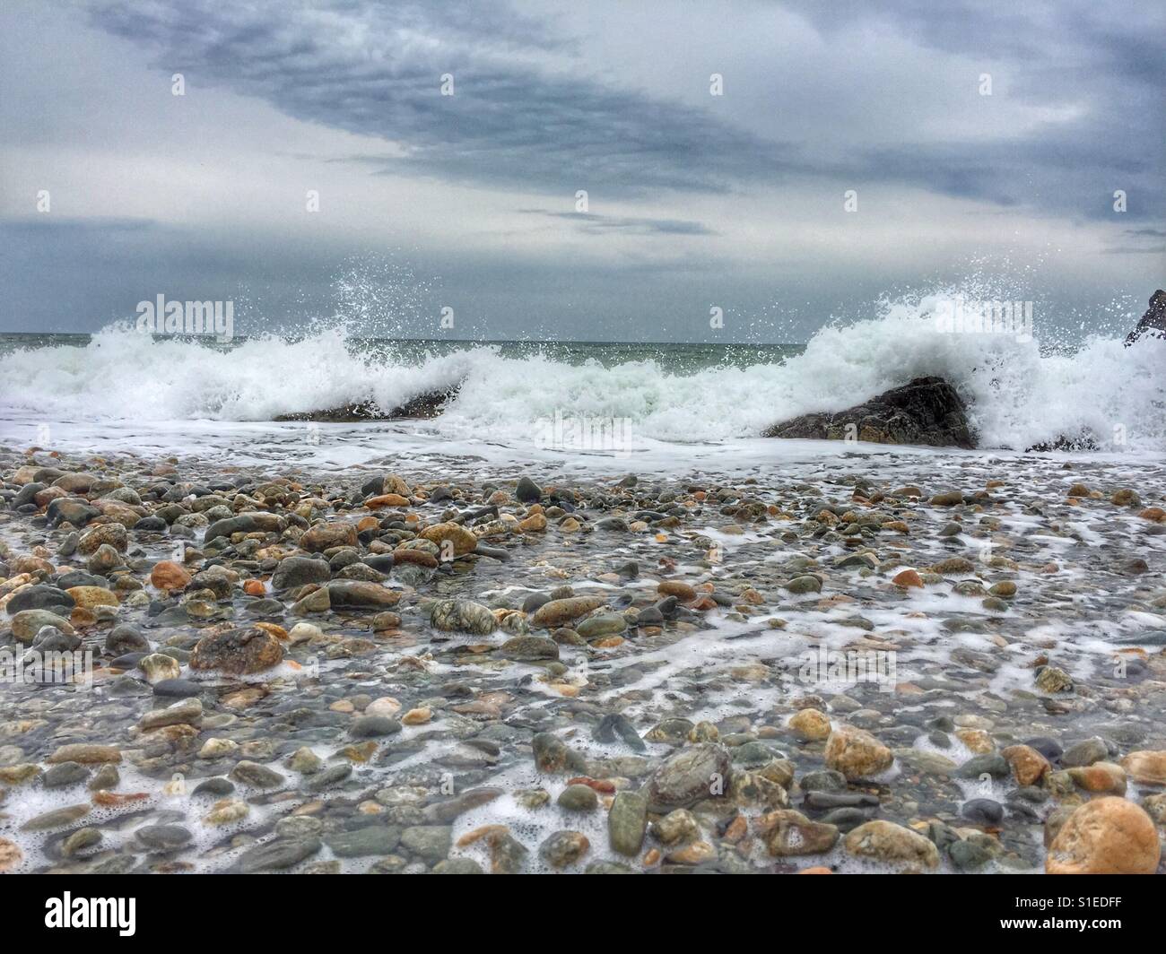 Waves breaking over rocks on pebbly beach - Smartphone Captured Stock Image