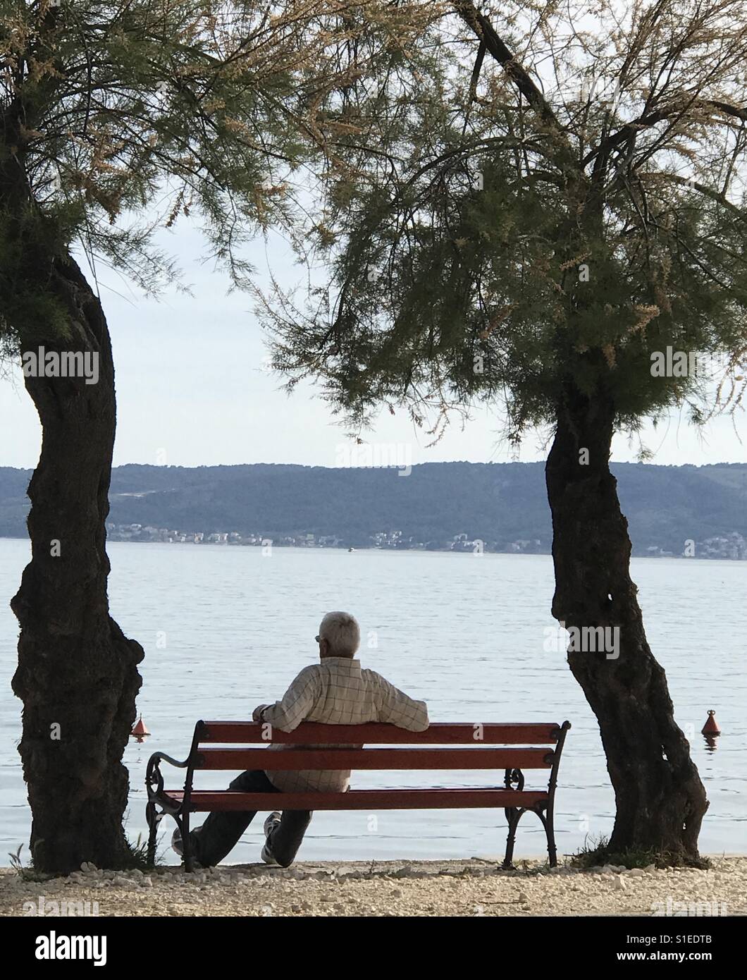 A pensioner enjoys his time at the bench by the Adriatic Sea in Kastela, Croatia - Smartphone Captured Stock Image