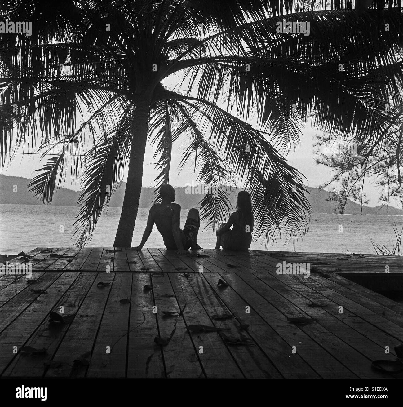 Black and white photo of the couple (silhouette) sitting under the palm tree - Smartphone Captured Stock Image