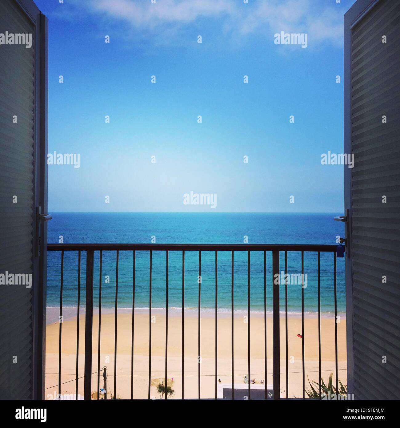 View of a golden sandy beach and blue sky with a small amount of white fluffy clouds from a beachside apartment in Cornwall. - Smartphone Captured Stock Image
