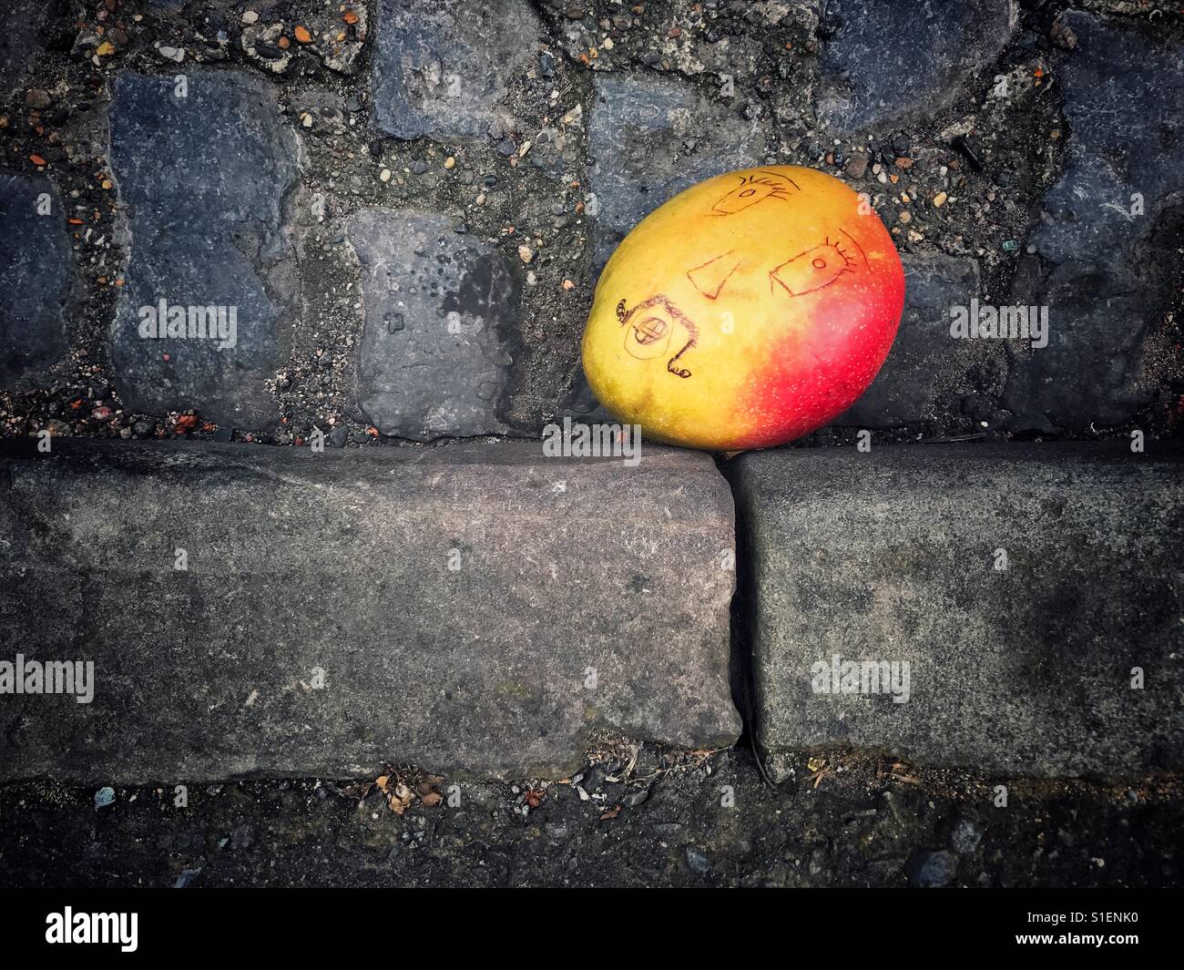 Mango with face drawn on it in the gutter of road Stock Photo