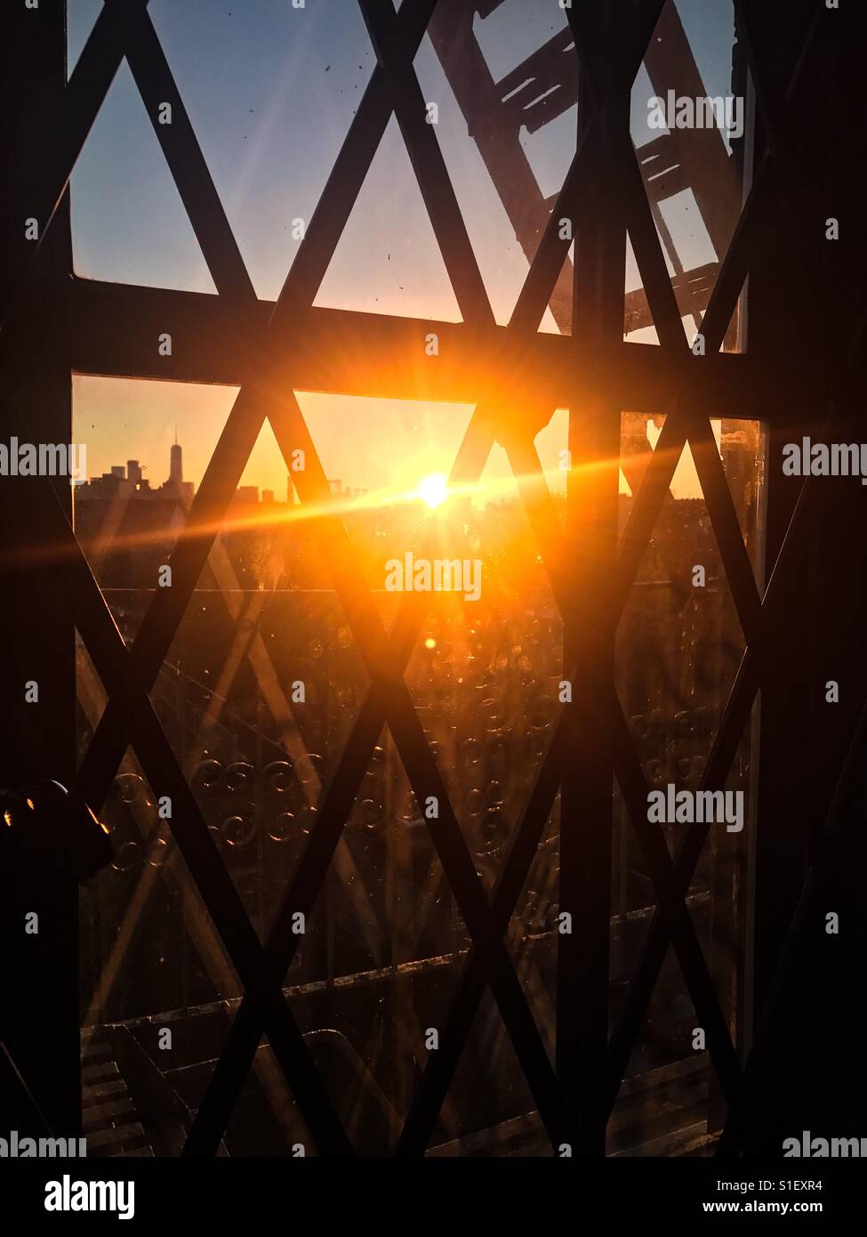 Sunset through a gated window in Brooklyn overlooking the Manhattan skyline. - Smartphone Captured Stock Image