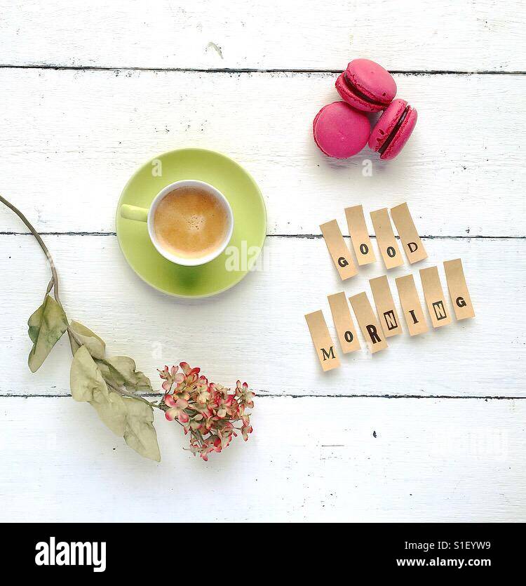 Lovely tabletop composition with cup of coffee, flowers, macarons and good morning quote Stock Photo