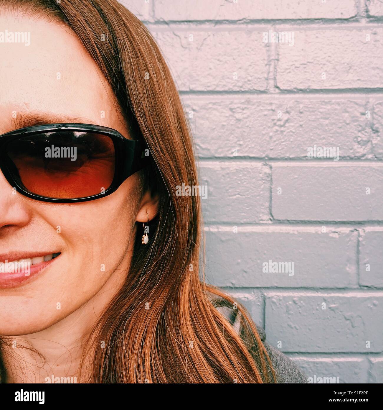 A cropped close up portrait of a smiling 40 something female shot against a brick background Stock Photo