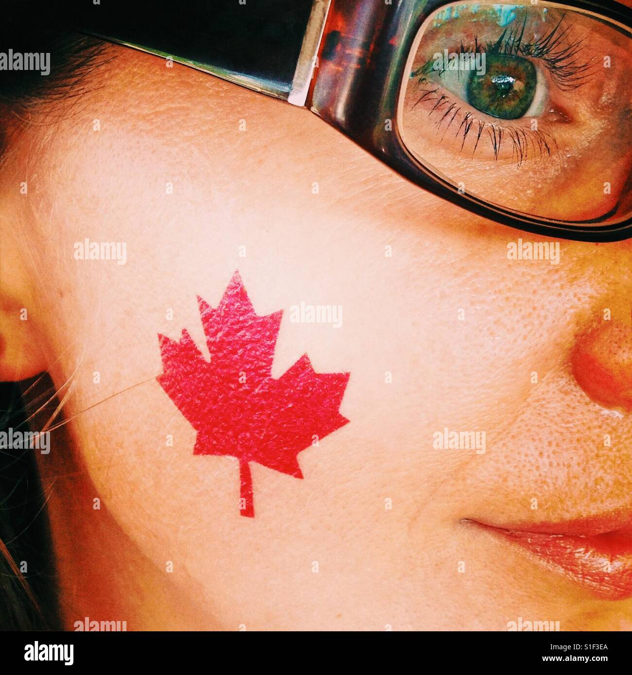 A close-up of a girl with a temporary maple leaf tattoo on her cheek Stock Photo