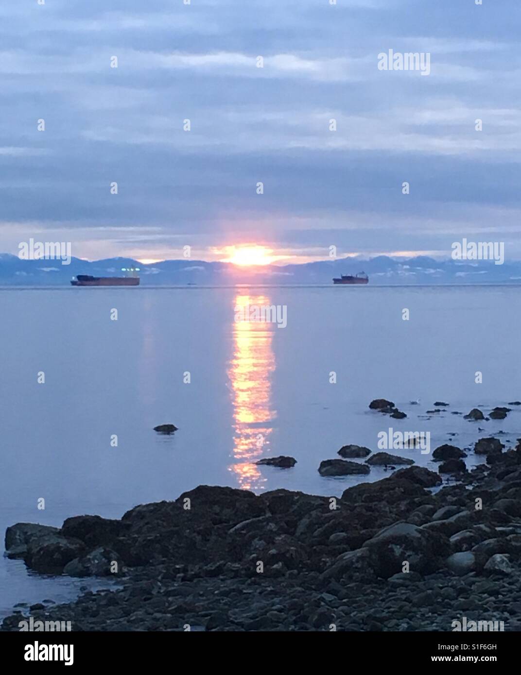 Beautiful sunset reflection in the ocean with cargo boats and mountains ...