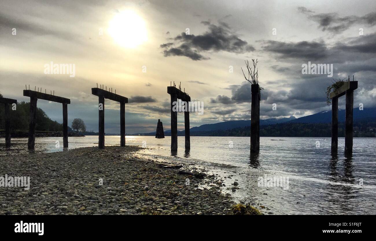 Sun and clouds behind a ruined pier in British Columbia Stock Photo