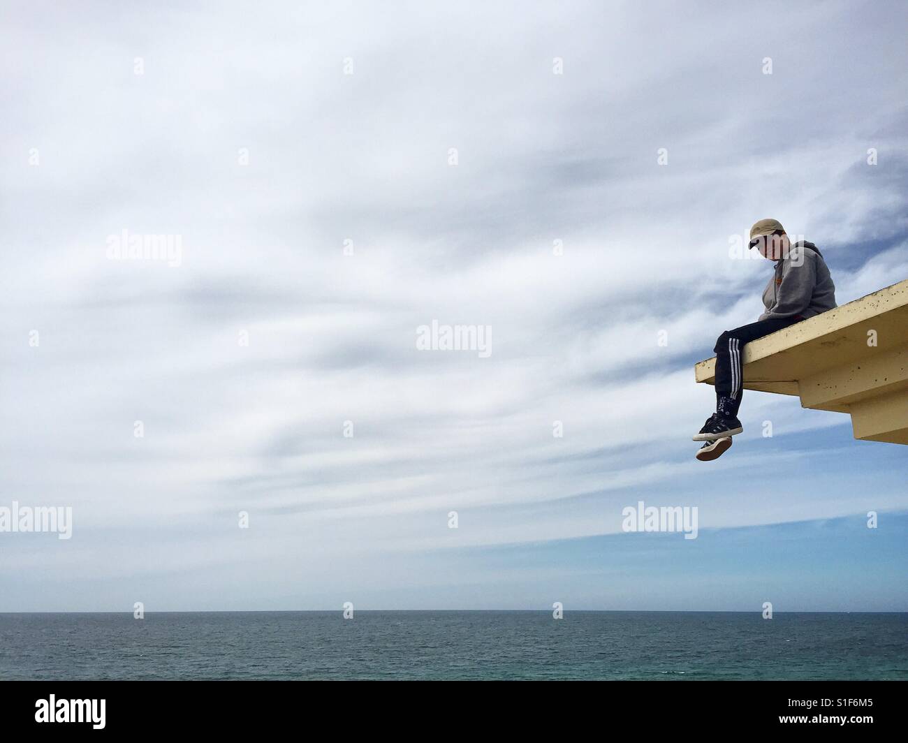 Teenager sitting on a roof overlooking the sea, France. Stock Photo