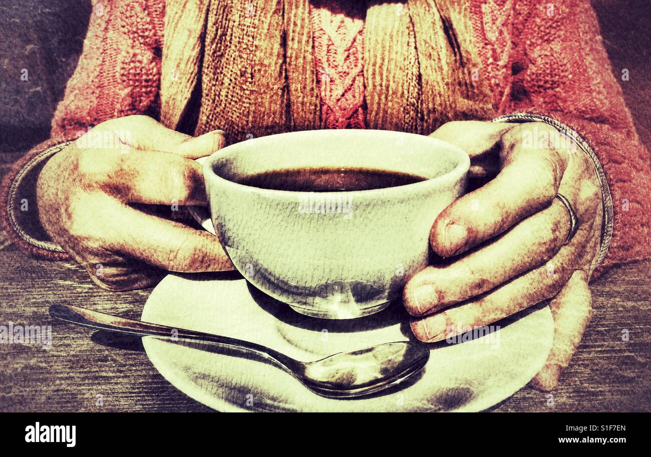 Woman holding a hot drink, seated at a table - Smartphone Captured Stock Image