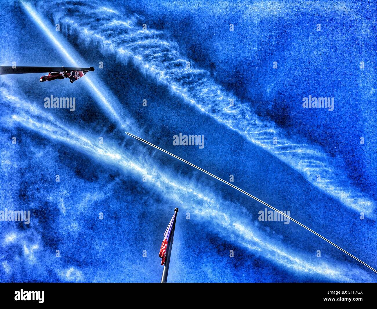 Vapour trails and flags (Union Jack and The British Library) against blue sky, low angle view - Smartphone Captured Stock Image