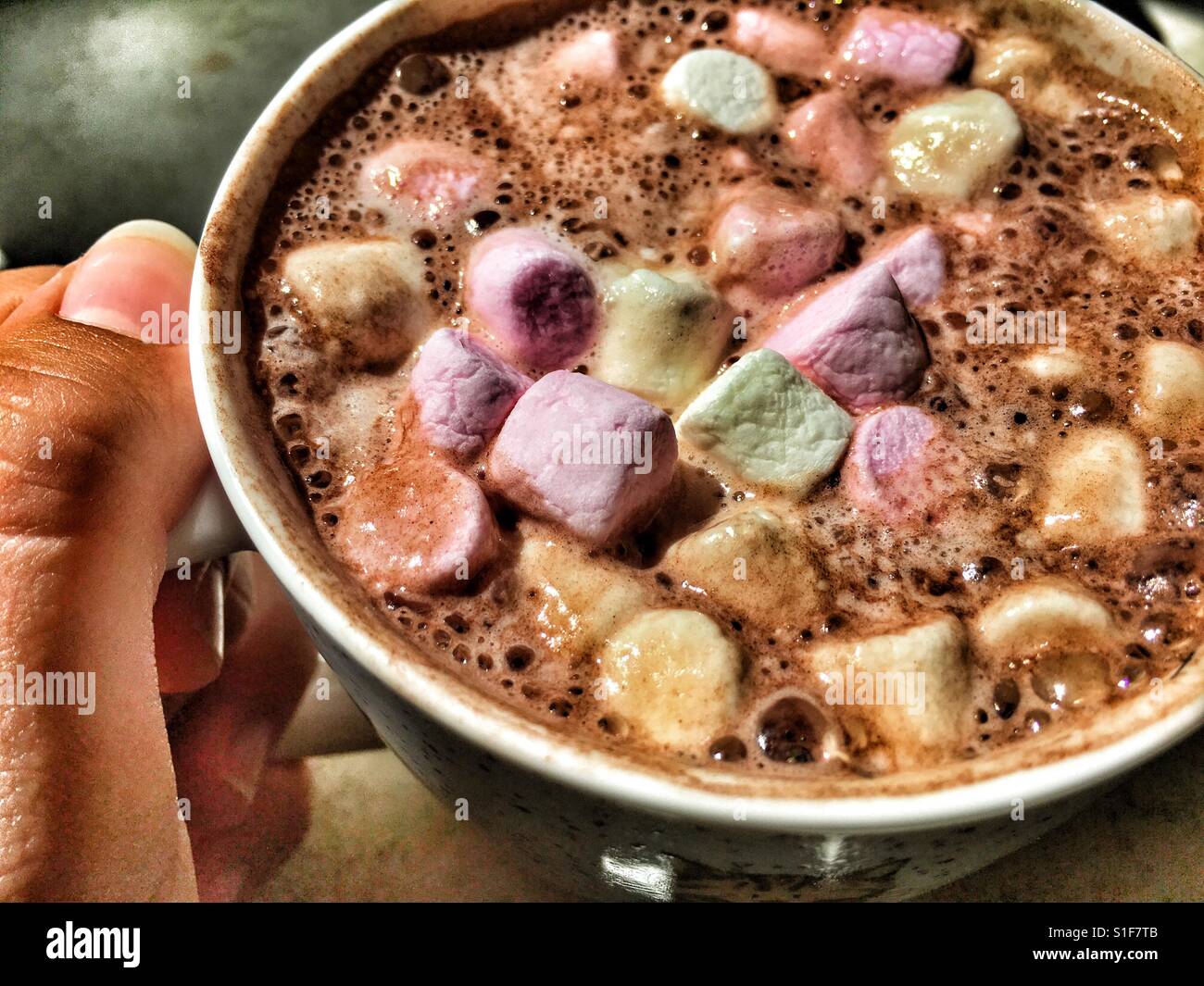 Mug of hot chocolate topped with mini marshmallows in teenage girl's hand - Smartphone Captured Stock Image