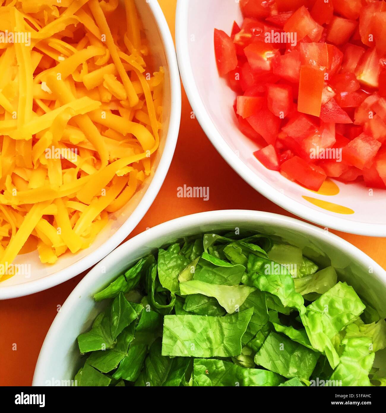 Three bowls containing grated cheese, diced tomatoes and lettuce Stock Photo