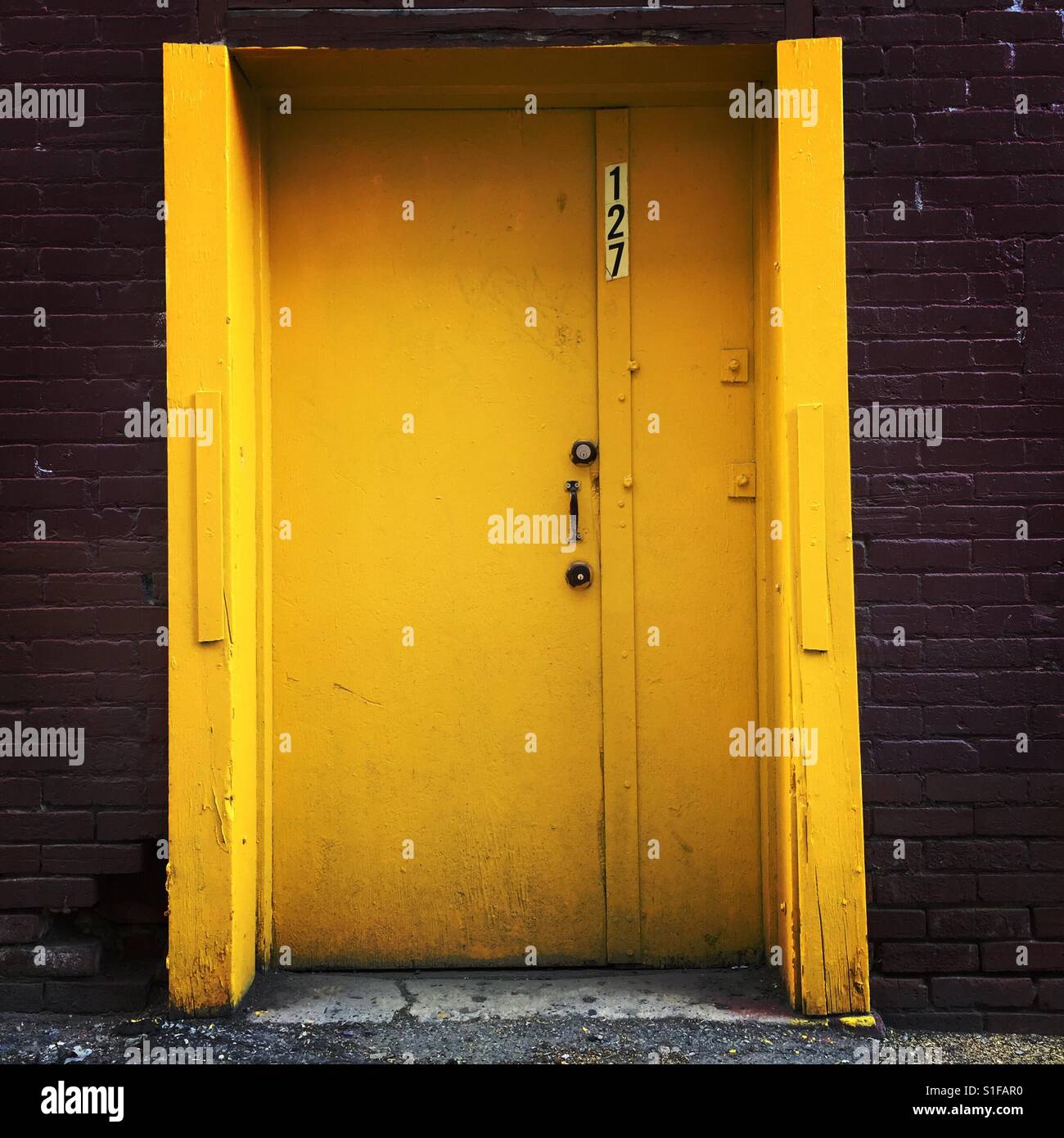 The number 127 on a yellow door surrounded by a brick facade Stock Photo