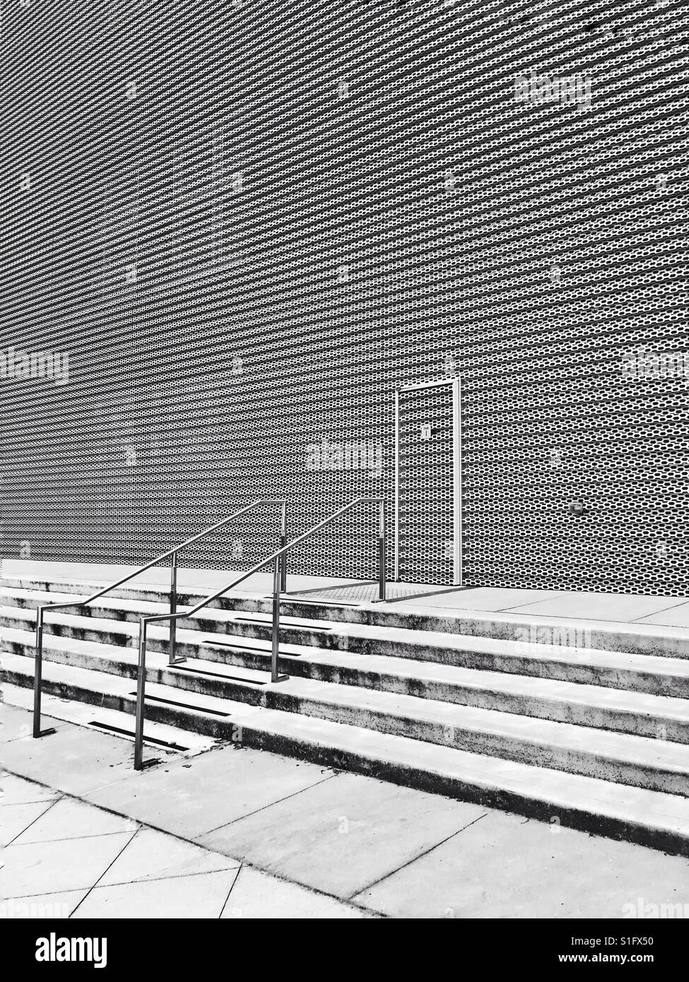 An exterior wall made of metal with small patterns of holes to let the light in but give the people inside the building privacy. - Smartphone Captured Stock Image