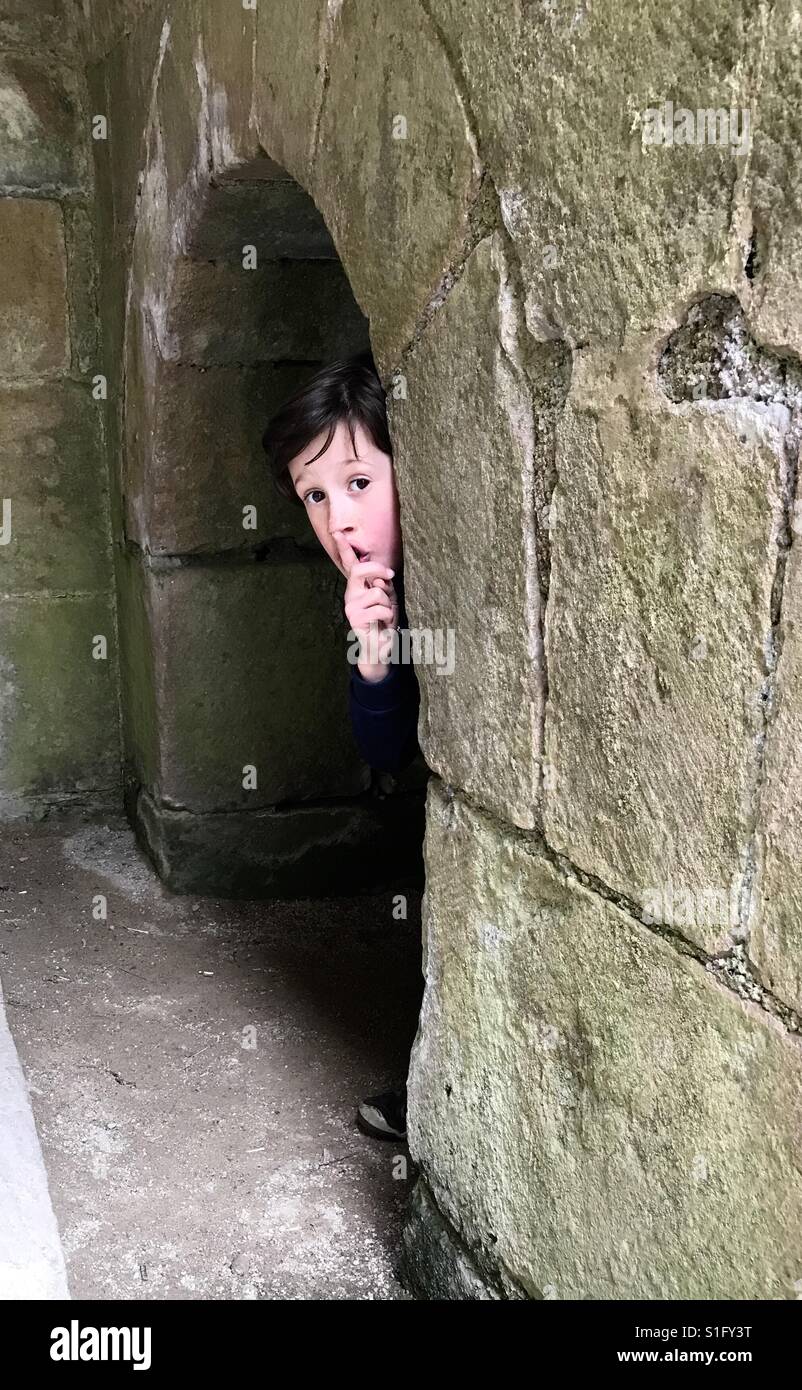 A young boy plays hide and seek in an ancient stone archway. Stock Photo