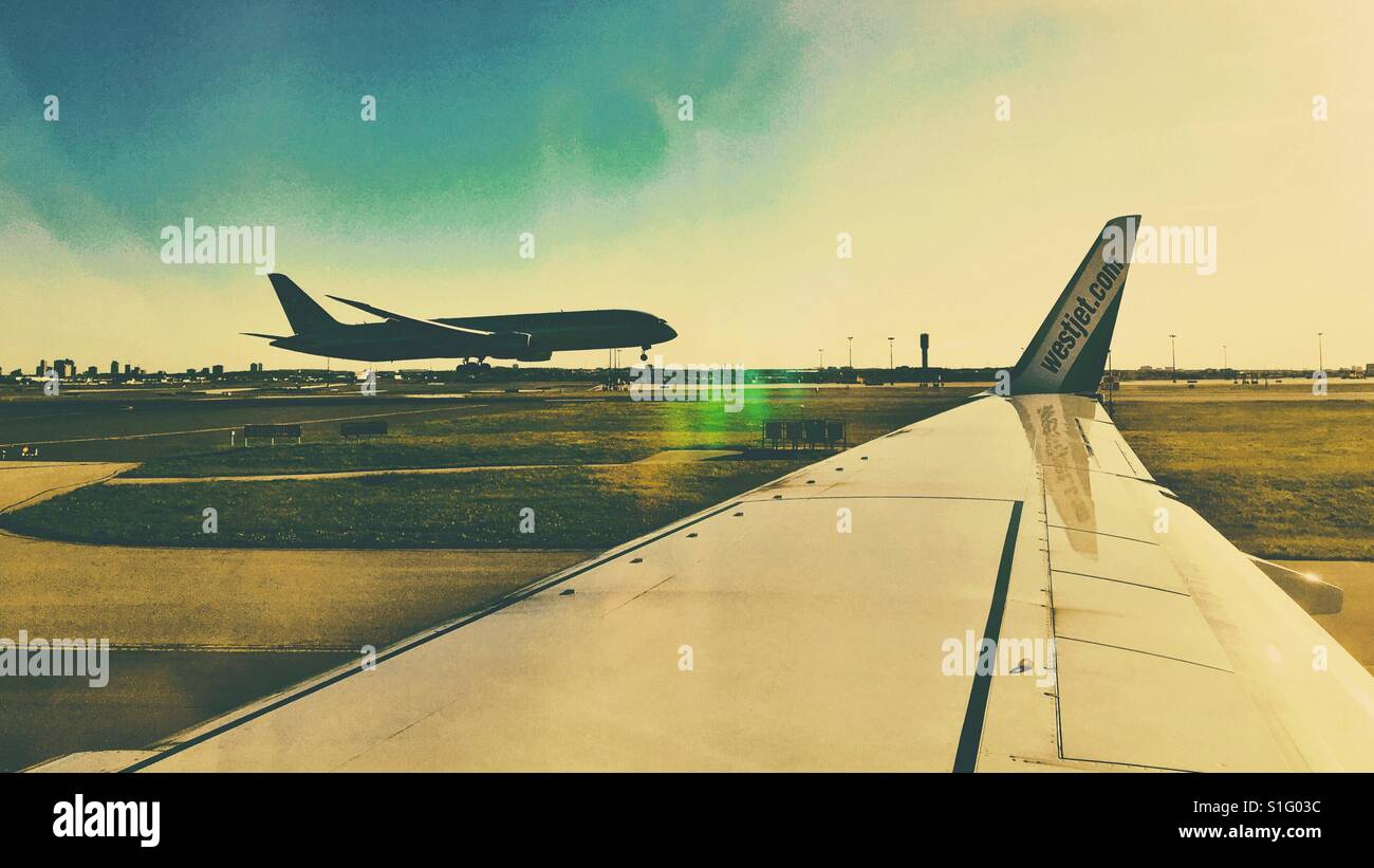 Looking out the window of a taxiing airplane on the runway, watching another plane land. - Smartphone Captured Stock Image