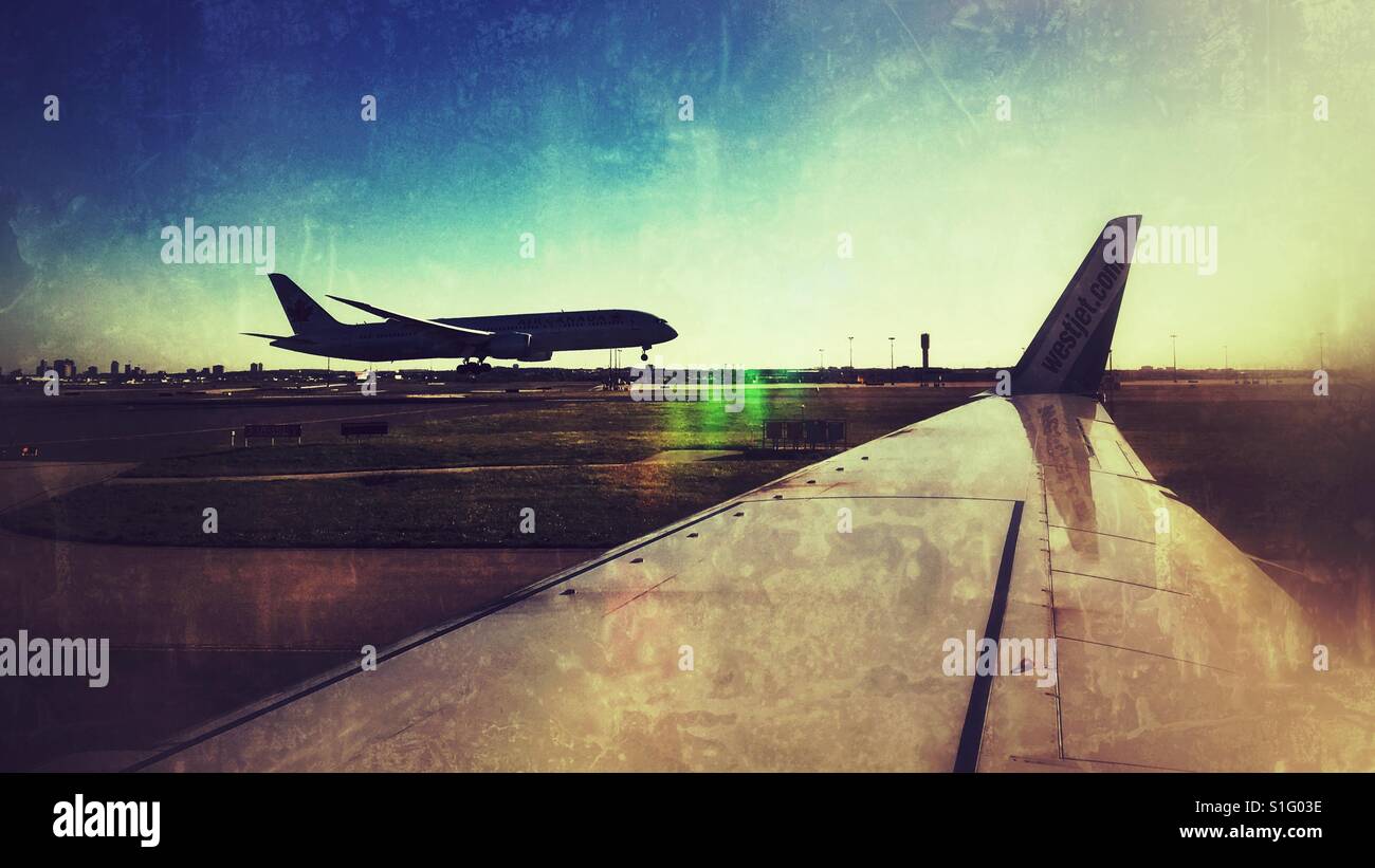 Looking out the window of a taxiing airplane, watching another airplane land in the late afternoon sunshine. - Smartphone Captured Stock Image