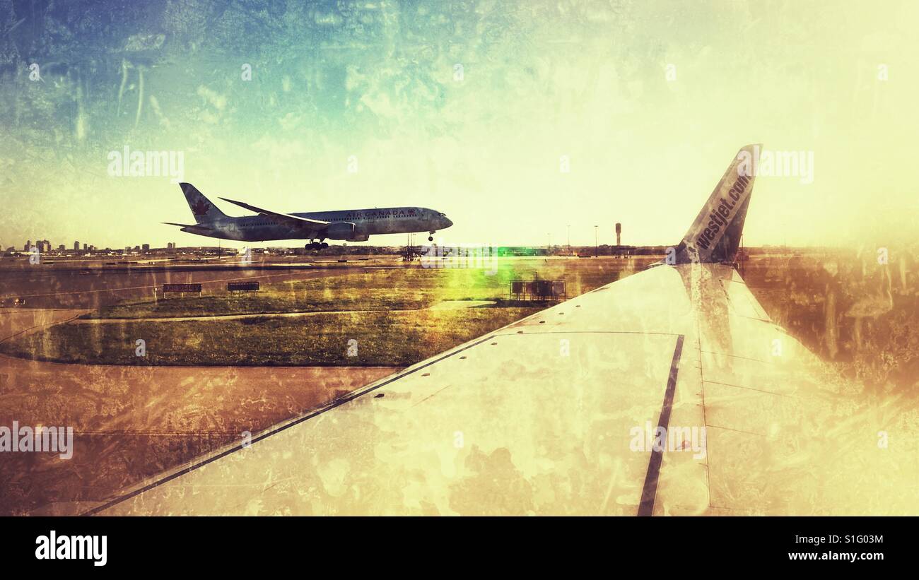 Looking out of a plane window over the wing, watching another airplane landing on a sunny evening. Distressed edit. - Smartphone Captured Stock Image