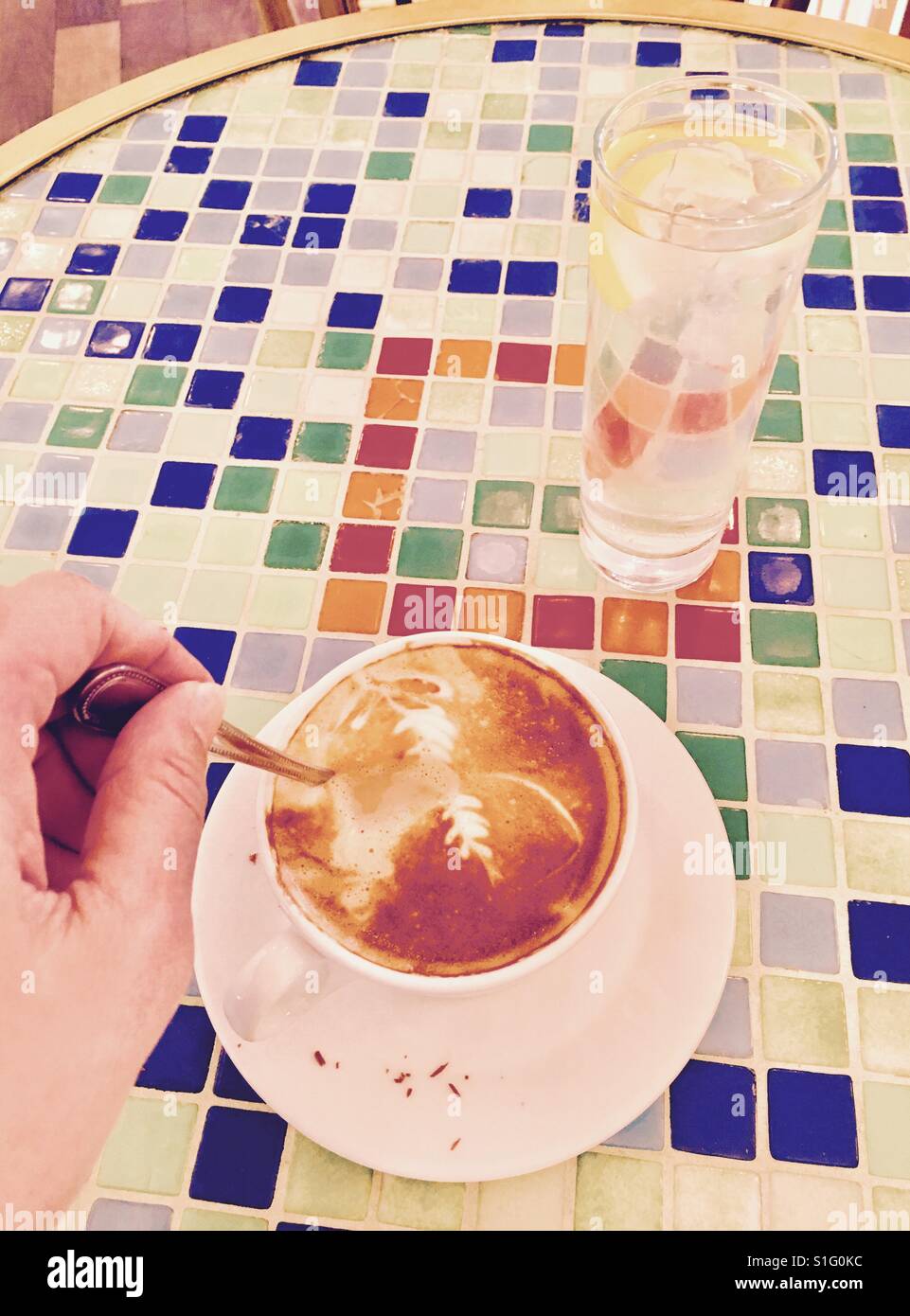 Stirring flat white and a glass of water against mosaic background - Smartphone Captured Stock Image